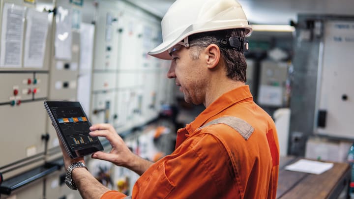 Technician in a control room on a ship looking on an ipad with ecomate screen Technician in a control room on a ship looking on an ipad with ecomate screen
